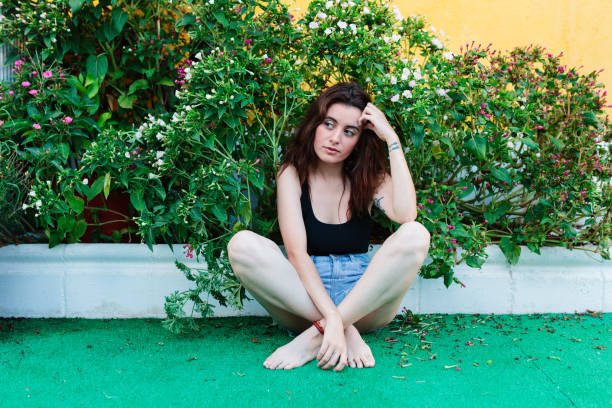 Portrait of beautiful young woman with dyed blue hair and a ponytail wearing a long sleeved crop top short jeans and high heels kneeling on a white background