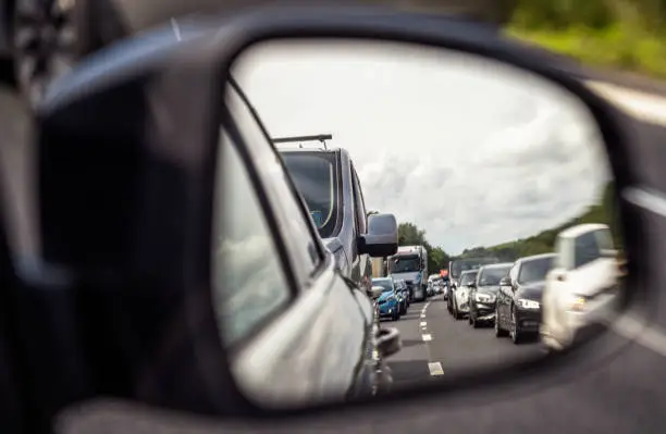 A view in a car's wing mirror showing a dual carriageway filled up with a traffic jam on a busy day.