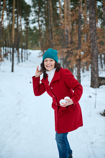 Beautiful cheerful woman in bright colorful warm winter clothes plays snowballs in a snowy forest. Happy young lady having fun, playing snowballs, enjoying her weekend outdoor on a beautiful cold day