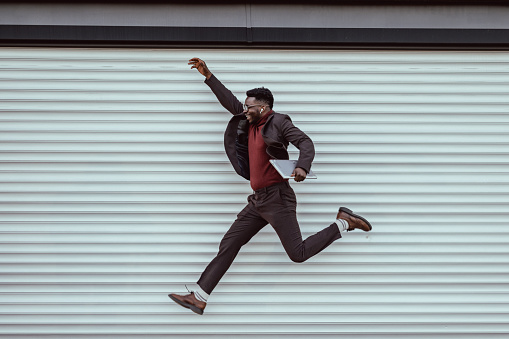 Young African-American businessman jumping and holding a laptop