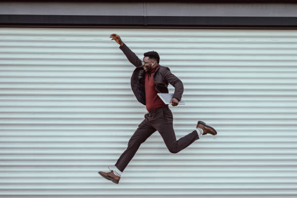 Happy young businessman jumping Young African-American businessman jumping and holding a laptop jumping stock pictures, royalty-free photos & images