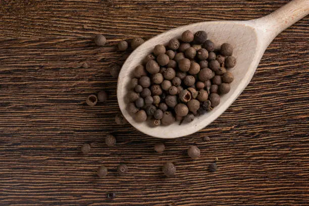 Allspice, pimento spice, Jamaican pepper in wooden spoon wooden background.