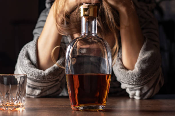 女性のアルコール依存症。女性の女性はテーブルに座っている 自宅でアルコールボトルを飲む 悲しい 一人でアルコール依存症 兆候と症状 リハビリテーション 虐待と回復の問題 - senior adult loneliness one person sadness ストックフォトと画像