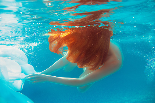 Portrait of smiling young beautiful red-haired girl in sunny day in open swimming pool in summer underwater