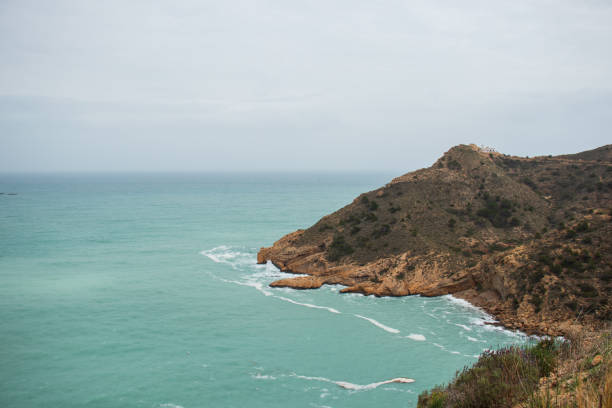 Cape entering the Mediterranean Sea with the lighthouse of Albir on the highest part of the rocky mountain. Protected natural area in the municipality of Alfaz del Pi. Mediterranean landscape.