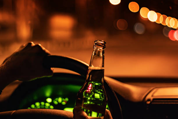 istock Drinking beer while driving car. Man hold bottle alcohol in hand at the night 1388208759