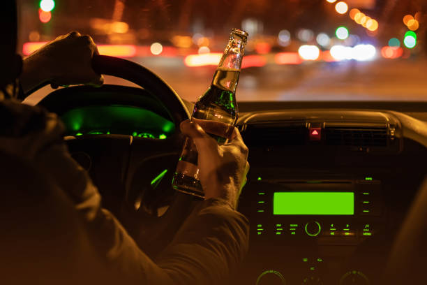 пить пиво за рулем автомобиля. мужчина держит бутылку алкоголя в руке ночью - designated driver стоковые фото и изображения