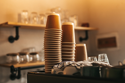 Close-up stack of upside down disposable cups. Interior of illuminated coffee shop.