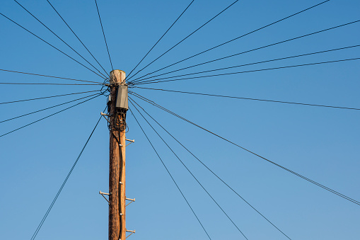 Low angle view of a wooden telephone pole with multiple wires coming form it in multiple directions in the North East of England.