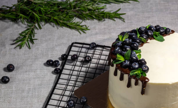 istock Sponge white cake decorated with chocolate with blueberries on top, stands on golden substrate. Image for website about food, confectionery. Selective focus. 1388227610