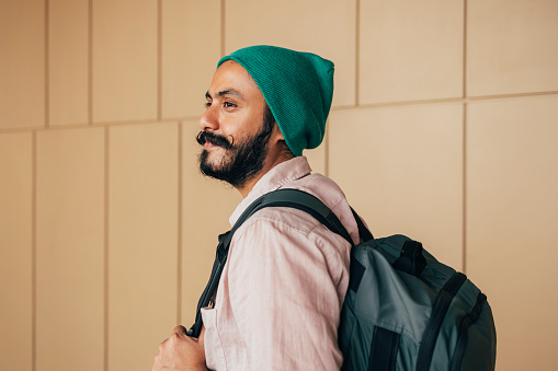 A handsome Indian male hipster with a green beanie smiling while thinking about something.