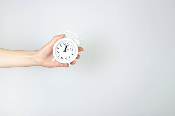 istock Partial view of hand holding alarm clock. Creative Time concept minimal style. 1388230125