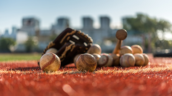 Baseball bat, glove and balls on synthetic ground in a sunny morning.