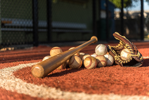 Baseball bat, glove and balls on synthetic ground in a sunny morning.