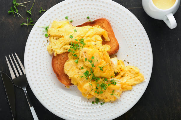 istock Scrambled Eggs. Fluffy and Buttery scrambled eggs on bread with microgreen radish and hollandaise sauce on white plate over dark old wooden background. Homemade breakfast or brunch meal. Top view. 1388232394