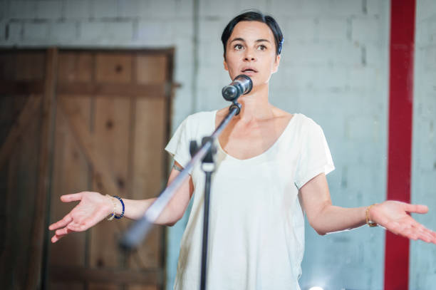 Smiling and witty stand up actor comedian on stage, talking and singing Smiling and witty female stand up actor comedian on stage, talking and singing into a microphone and making the audience laugh. Final rehearsal before the premiere and performance in the theater actress audition stock pictures, royalty-free photos & images