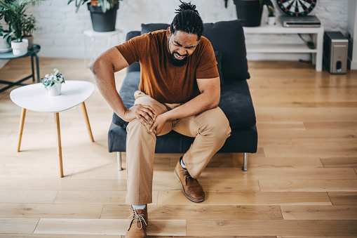 People, health care and problem concept - unhappy mid adult man suffering from knee ache at home