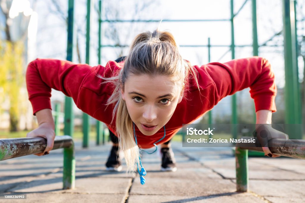 Sporty young woman in sportswear doing bar push-ups looking at camera Sporty young fit woman in sportswear doing bar push-ups Concentration Stock Photo
