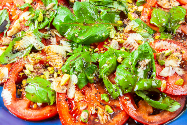 Tomato and basil salad Salad of fresh tomato slices with basil, garlic, pistachios, baslsamic vinegar and olive oil. Blue Spice Basil stock pictures, royalty-free photos & images