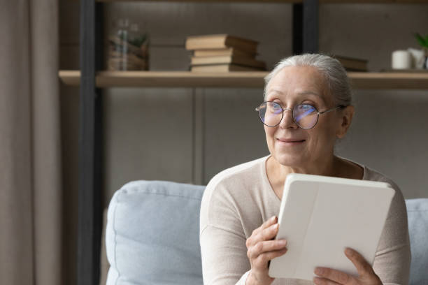 istock Smiling elderly tablet user sitting on couch in good thoughts 1388244198