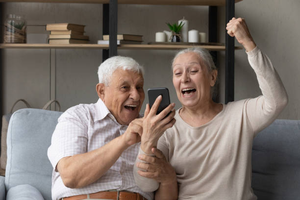 istock Excited cheerful elder couple using smartphone, making winner gesture 1388244217
