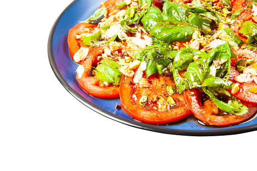 Salad of fresh tomato slices with basil, garlic, pistachios, baslsamic vinegar and olive oil isolated on white background.
