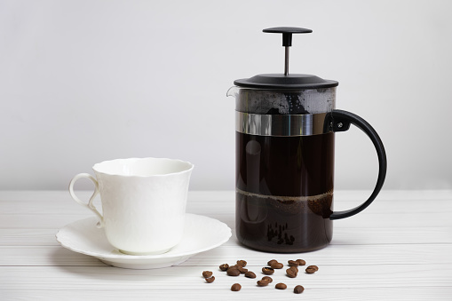 French-pressed ground coffee and a white porcelain cup and saucer. Preparing ground coffee in a press. Refreshing drink for breakfast.