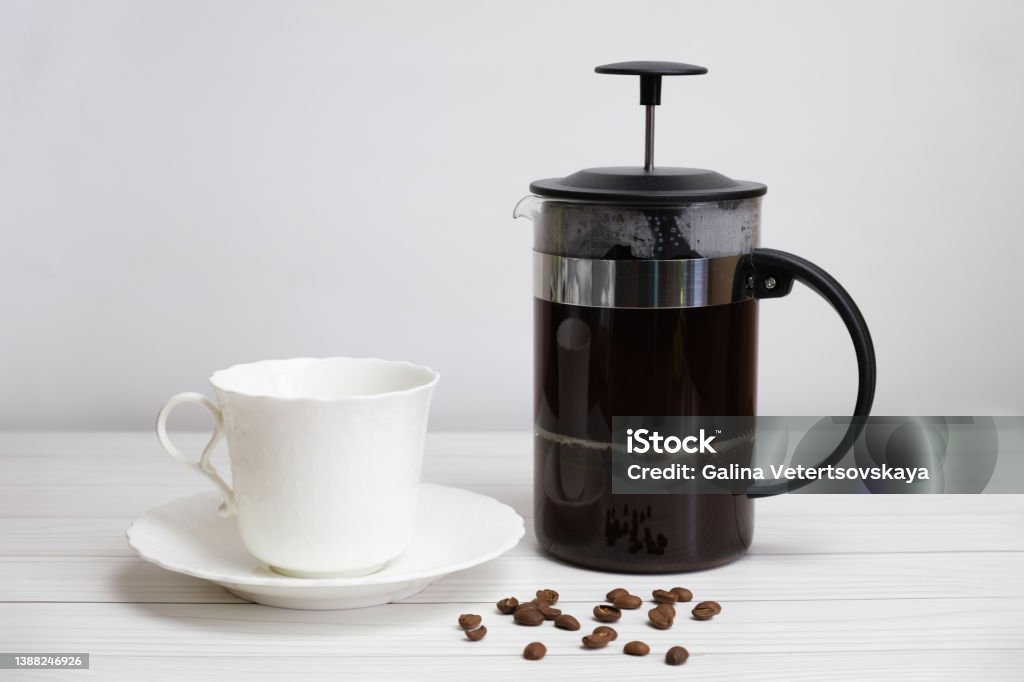 French-pressed ground coffee and a white porcelain cup and saucer French-pressed ground coffee and a white porcelain cup and saucer. Preparing ground coffee in a press. Refreshing drink for breakfast. French Press Stock Photo