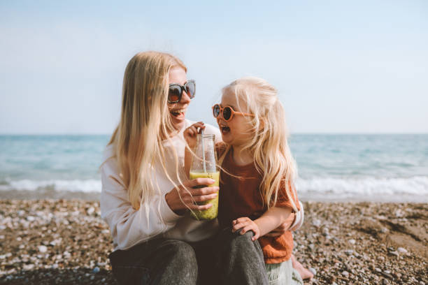 семья мать и дочь ребенок пьют смузи на пл�яже здоровый образ жизни веганская органическая пища путешествия каникулы летние каникулы на све - fun mother sunglasses family стоковые фото и изображения