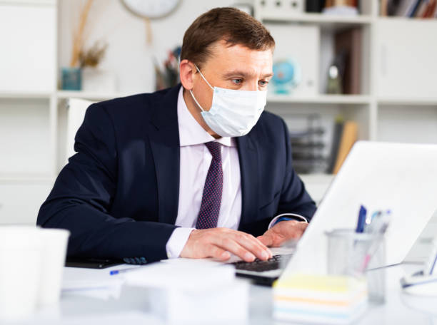 istock Manager in medical mask working on laptop in office 1388248371