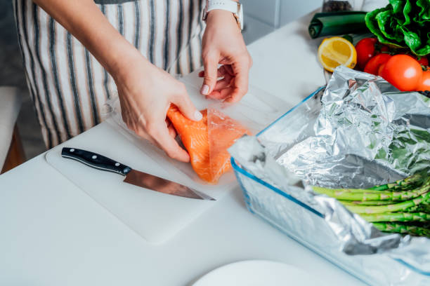 baked salmon with green asparagus recipe steps. step one. woman planning to slice fresh salmon on cutting board. step by step recipe. healthy cooking at home in the kitchen according to recipe. - mature woman having fish bildbanksfoton och bilder