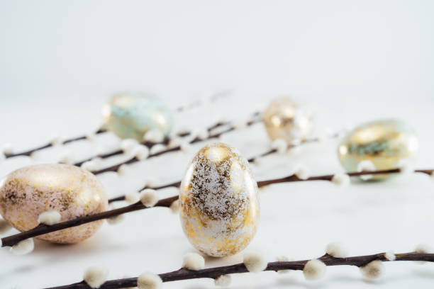 istock Blooming pussy willow branches and golden eggs in different patterns and colors on the white background. Minimalist, Modern Happy easter card. Selective focus, copy space. 1388248476