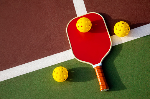 This is a photograph taken outside of a pickleball paddle and balls on a outdoor court