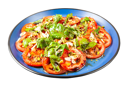 Salad of fresh tomato slices with basil, garlic, pistachios, baslsamic vinegar and olive oil isolated on white background.