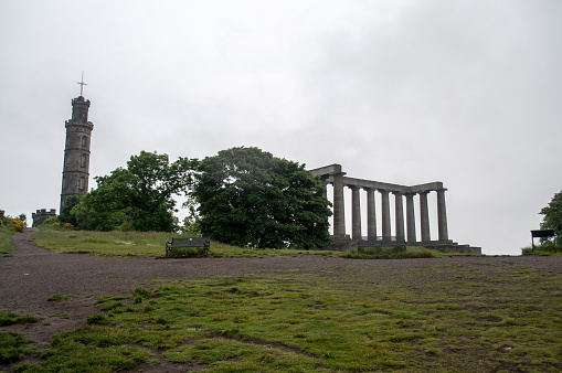 Old memorial buildings on Calton Hill above the city of Edinburgh in Scotland. Cloudy rainy sky in the city.
