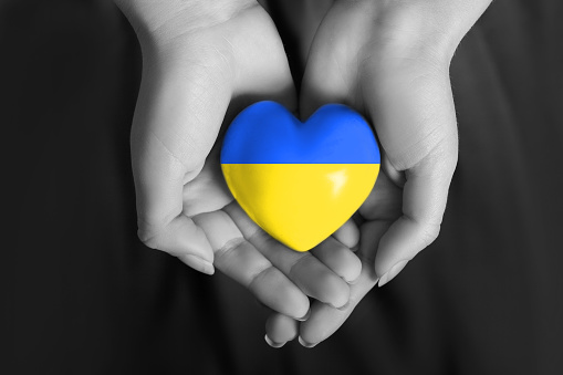 Women's hands hold a heart in the colors of the Ukrainian flag. pray for Ukraine. Stand with Ukraine.