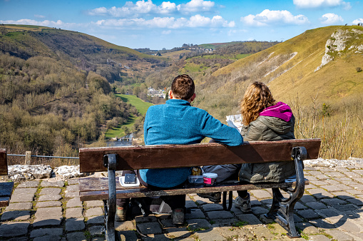 A couple of walkers sit on a bench at Monsal Head overlooking Monsal Dale to read a map. Monsal Head is in the Peak District National park in Derbyshire, UK.