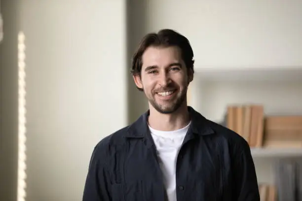 Positive successful millennial business professional man head shot portrait. Happy handsome confident young startup leader, company founder, posing in office, looking at camera with toothy smile