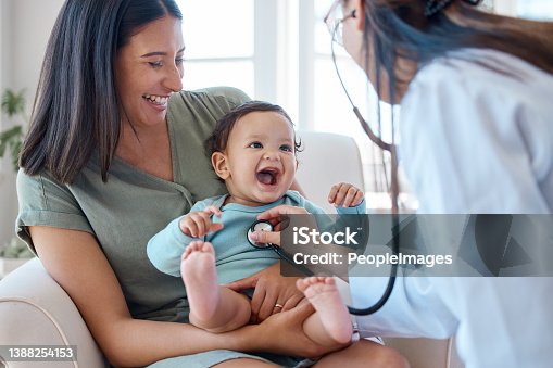 istock Shot of a baby sitting on her mother's lap while being examined by a doctor 1388254153
