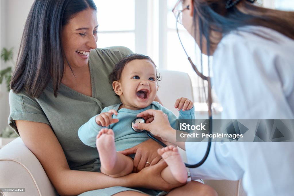 Shot of a baby sitting on her mother's lap while being examined by a doctor She's knows how to put a smile on your face Doctor Stock Photo