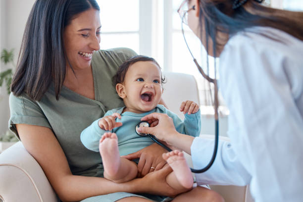 Shot of a baby sitting on her mother's lap while being examined by a doctor She's knows how to put a smile on your face pediatrician stock pictures, royalty-free photos & images