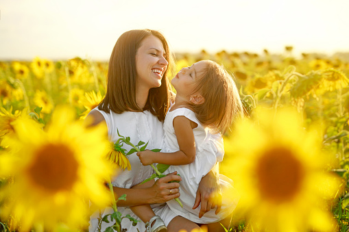 Mom and daughter are laughing merrily in a field with sunflowers. Tenderness, care and love of parents for children. Harmony and unity with nature. World Children's Day