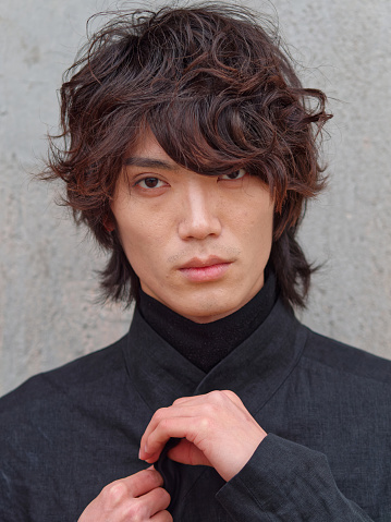 Portrait of handsome Chinese young man in black looking at camera with gray wall background, front view of confident young man, close up view head shot.