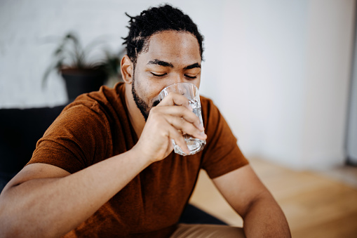 Water, drink and fitness with a sports man in a gym for exercise while taking a break to hydrate. Workout, training and drinking with a male athlete taking a sip from a bottle after his routine