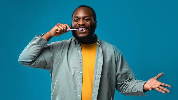 ritratto di uomo afroamericano in studio con sfondo blu colorato. la persona di colore si lava i denti con lo spazzolino da denti per uno stile di vita sano. le persone puliscono i denti usando le attrezzature dentali per la salute - dental hygiene elegance black toothbrush foto e immagini stock