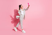 Photo portrait full body view of woman taking selfies on the go showing v-sign isolated on pastel pink colored background