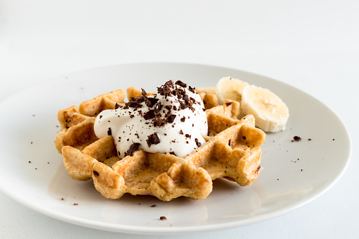 Delicious homemade oatmeal waffle with creamy natural yogurt, honey, banana and chopped chocolate on a white background.