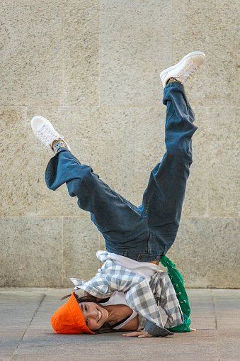 24-year-old dancer dressed in jeans, sleeveless t-shirt, checkered shirt, orange hat and white sneakers