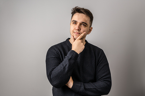 Portrait of one adult caucasian man 25 years old with short hair looking to the side in front of white wall background thinking wearing sweater copy space