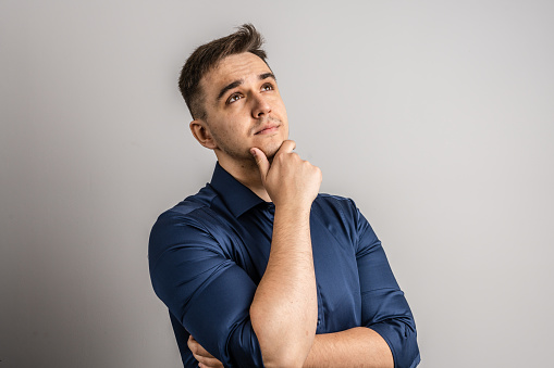 Portrait of one adult caucasian man 25 years old with short hair looking to the side in front of white wall background thinking wearing sweater copy space